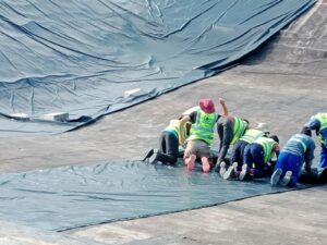 "Workers installing a dam liner in a rural area of South Africa. The liner is made of durable material and will help prevent water leakage and erosion in the dam